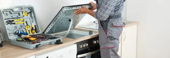 Cooktop repair technician lifting a built-in stovetop for service in Tempe, AZ