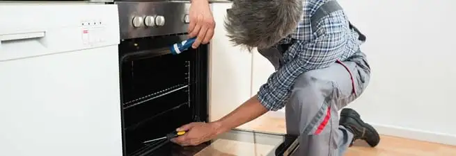 Oven repair technician inspecting and servicing an electric oven in Tempe, AZ