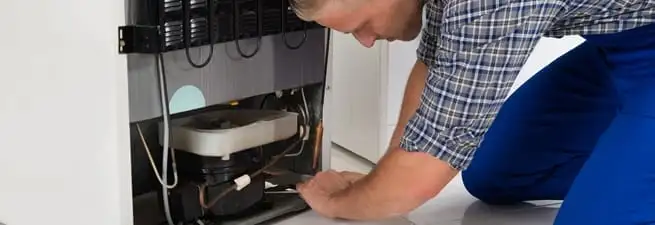 Refrigerator repair technician servicing the compressor and condenser area in Tempe, AZ